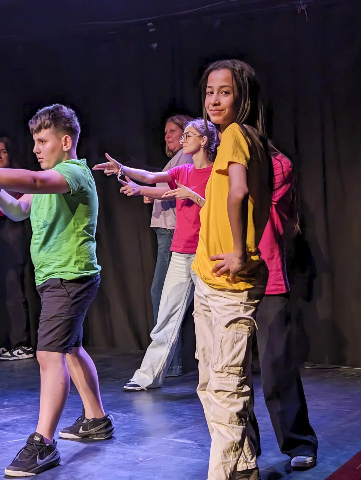 Jongeren in felgekleurde T-shirts dansen een choreografie op het podium
